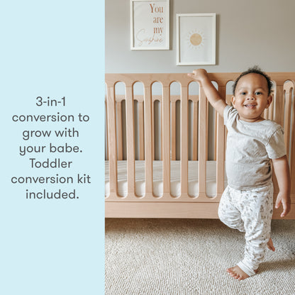 toddler standing next to newton galileo crib in natural color, text reads "3-in-1 conversion to grow with your babe. Toddler conversion kit included."