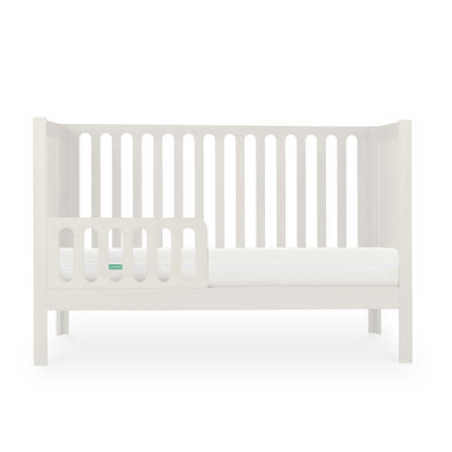 White modern baby crib with a Newton mattress visible, styled with minimalistic design on a plain background.