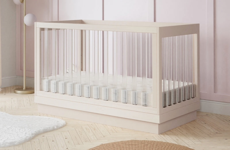Modern crib in a stylish baby room with light pink walls and wooden flooring.