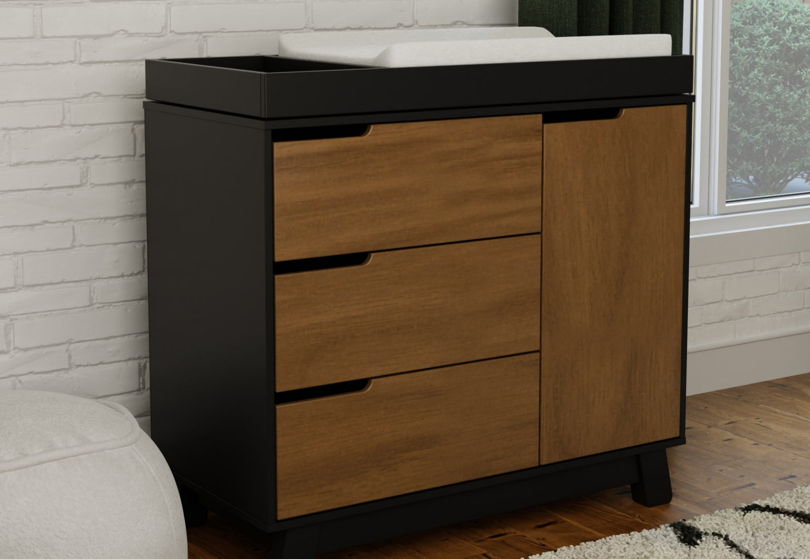 Stylish and functional nursery changing table with a dark base and natural wood drawers against a white brick wall.