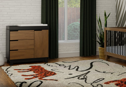 A stylish nursery room featuring a modern crib and changing table, decorated with a vibrant area rug and green curtains, showcasing a cozy and functional design.