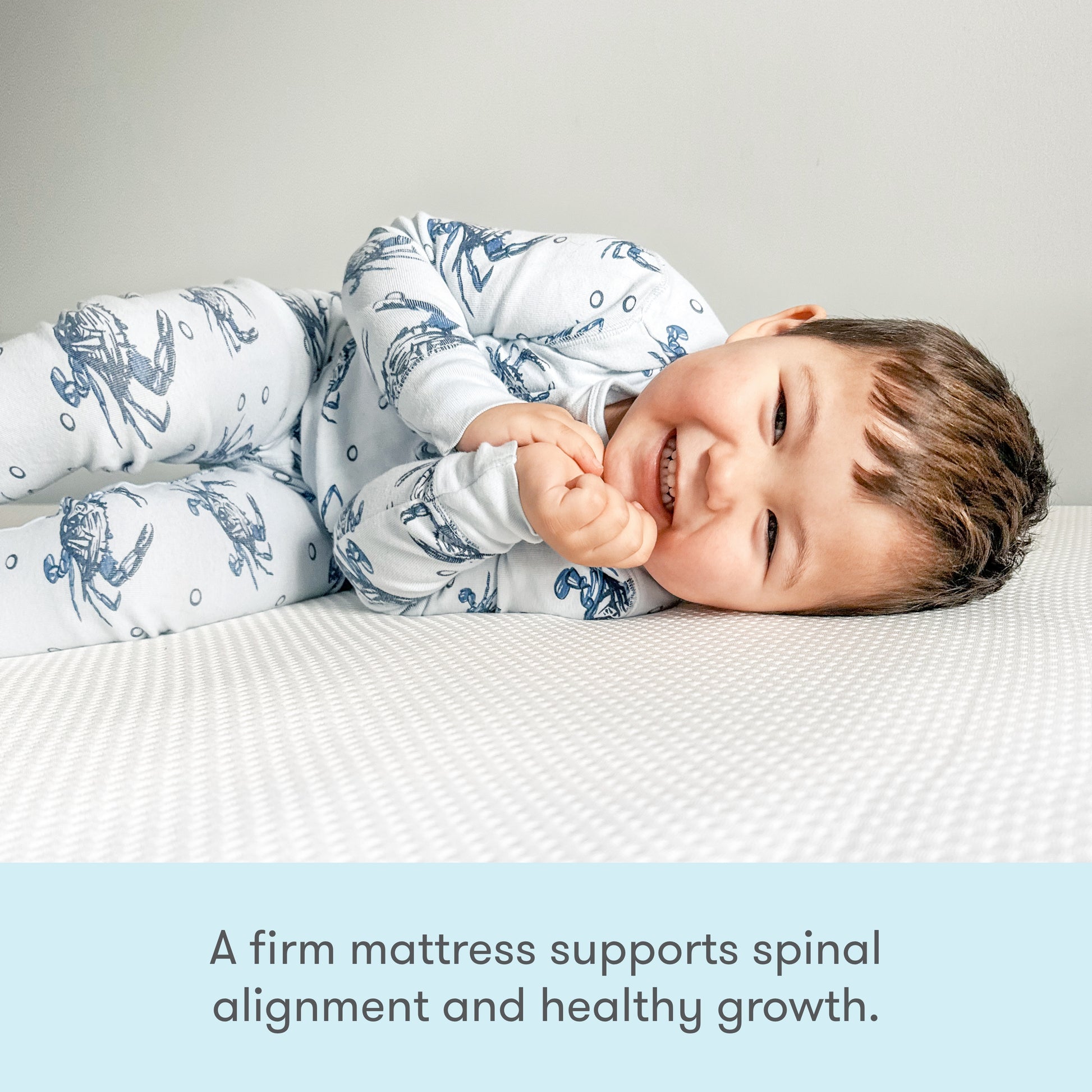 A smiling toddler in printed pajamas lies on a white mattress. Text below reads: The Newton Baby Kids' Twin Mattress is GREENGUARD Gold certified and firm to support healthy growth and spinal alignment.