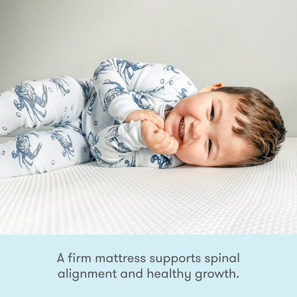 A smiling toddler in printed pajamas lies on a white mattress. Text below reads: The Newton Baby Kids' Twin Mattress is GREENGUARD Gold certified and firm to support healthy growth and spinal alignment.