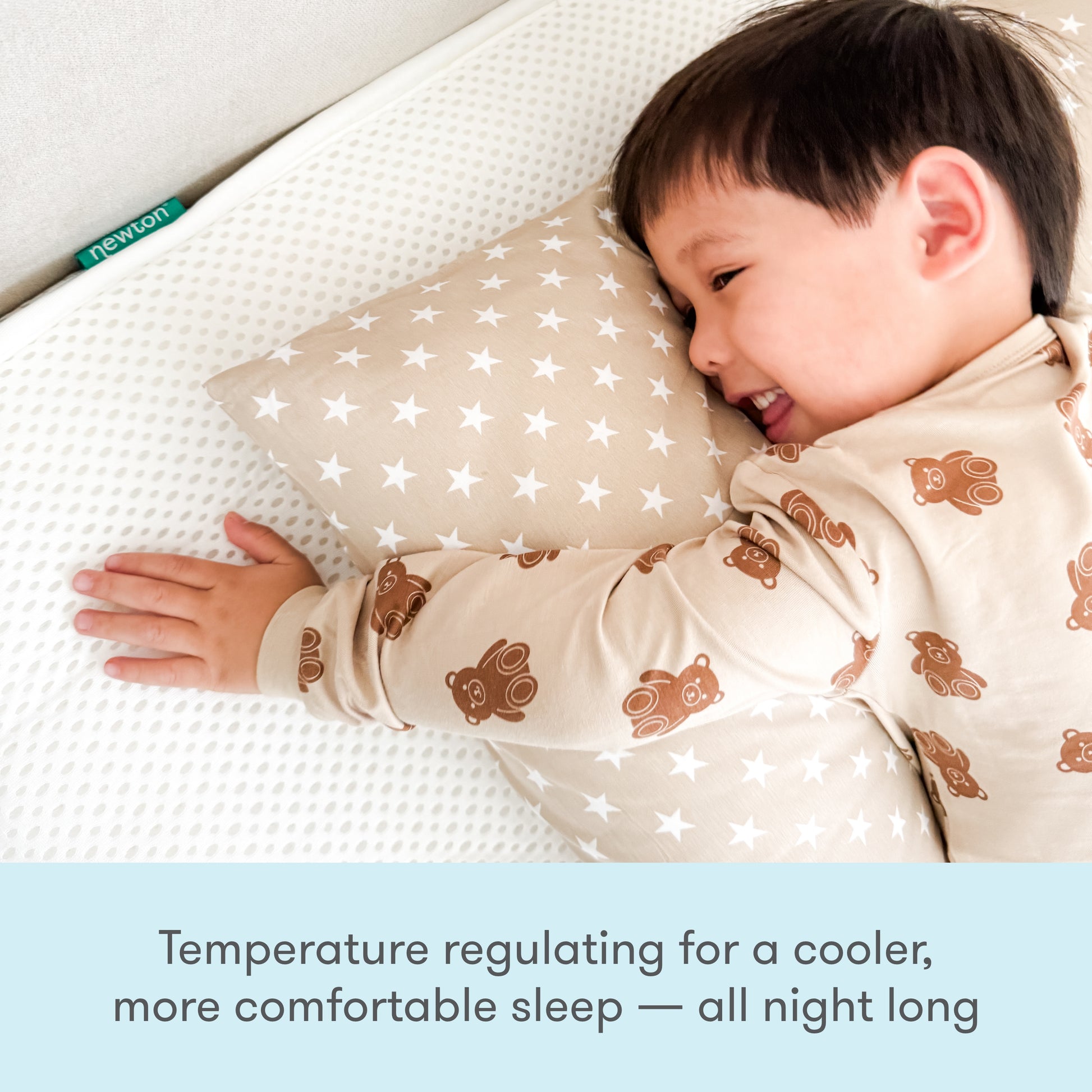 A child in bear-print pajamas hugs a star pillow while lying on the Newton Baby Kids' Twin Mattress. Text below: Temperature regulating for cooler, more comfortable sleep. GREENGUARD Gold certified for peace of mind.