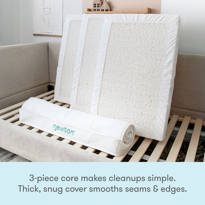 The Newton Baby Kids' Twin Mattress is shown with its 3-piece washable core and a rolled cover on a bed frame. GREENGUARD Gold certified, the textured white core and thick, snug cover make cleanups easy and edges smooth.