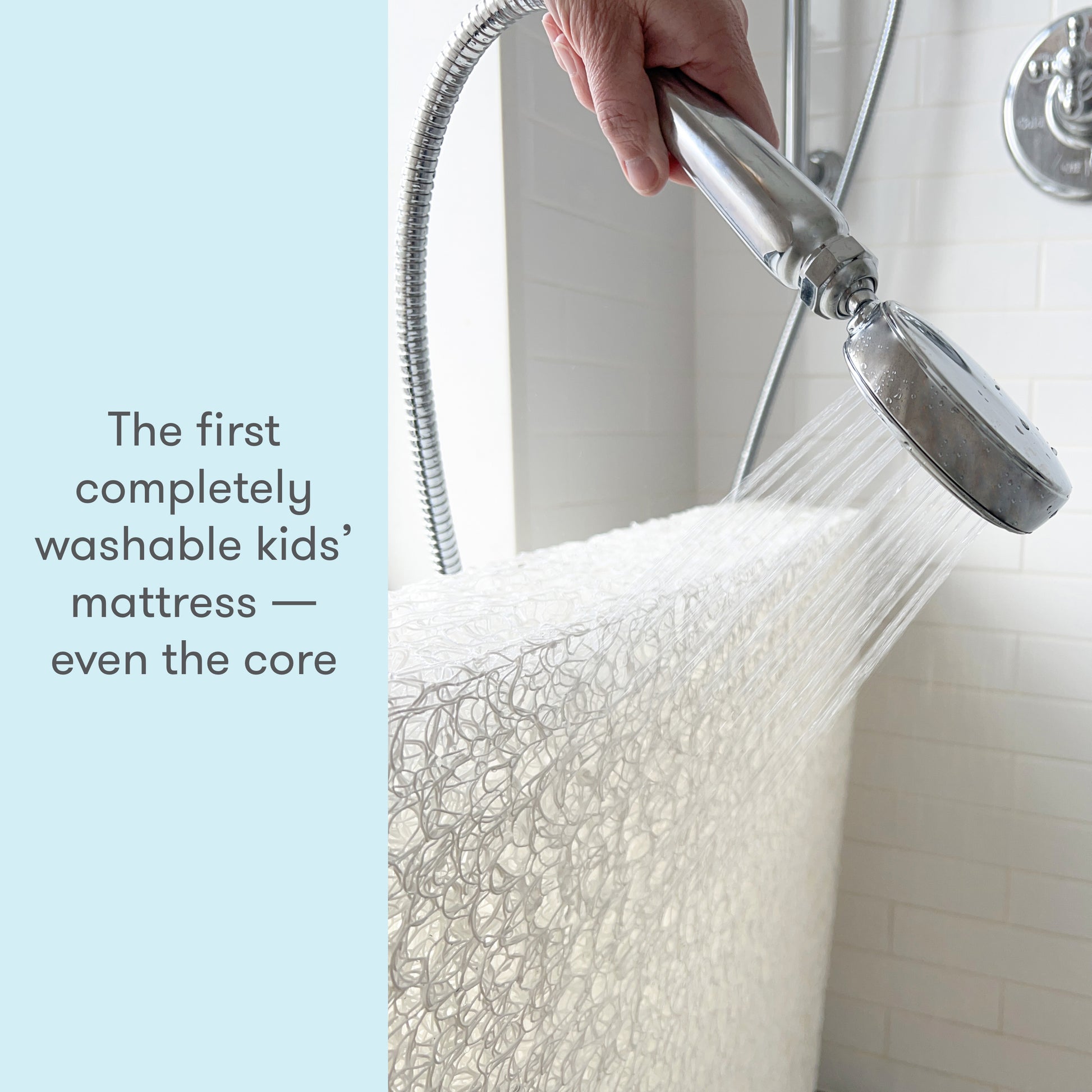 Hand washing a kid's mattress with a shower head in a white tiled bathroom, featuring text "The first completely washable kids’ mattress — even the core."