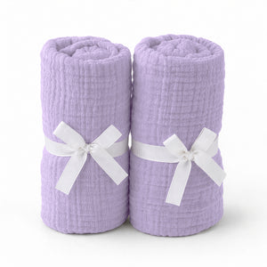 Two lavender sheets, rolled and tied with white ribbons, stand side by side on a white background—an ideal match for Newton Baby’s Breathable, Organic Cotton Sheets (2-pack) in any nursery. skip