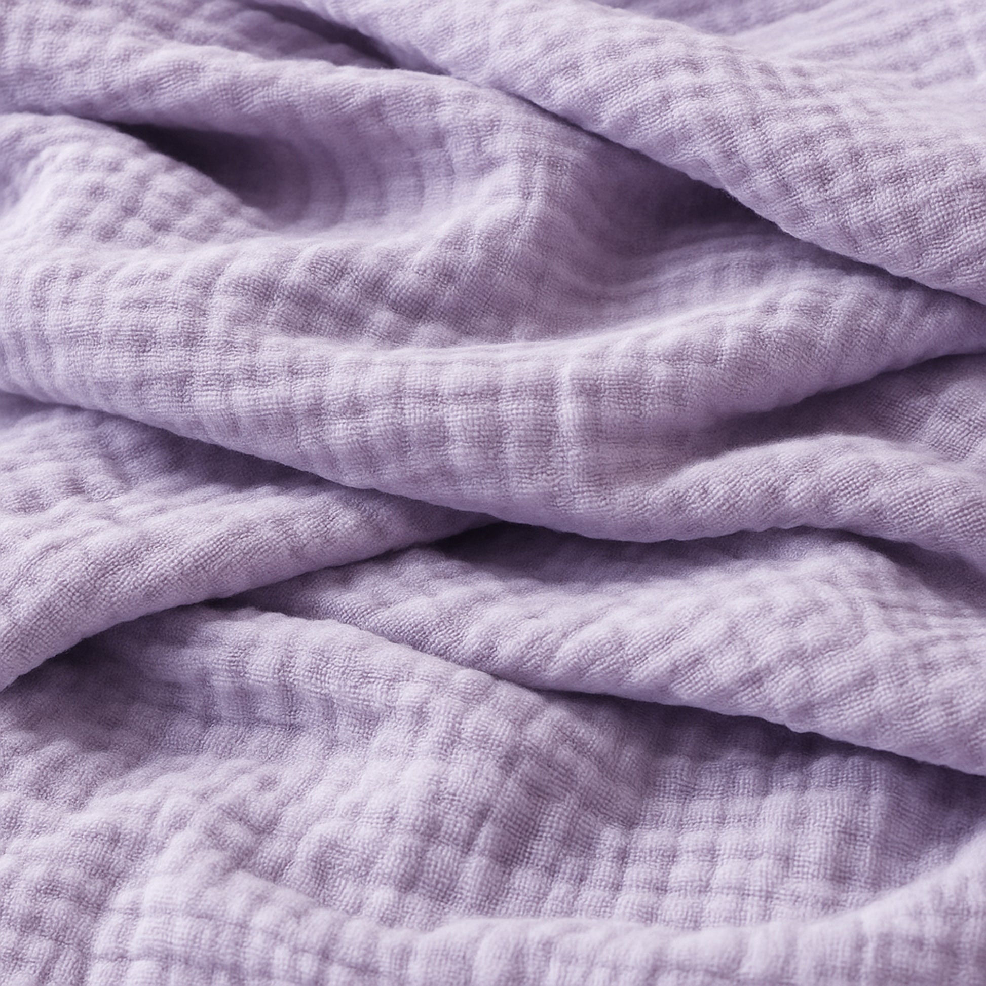 Close-up of soft, textured lavender fabric—like that in Newton Baby’s Breathable, Organic Cotton Sheets (2-pack)—featuring a slightly crinkled surface, subtle grid pattern, and gentle folds.