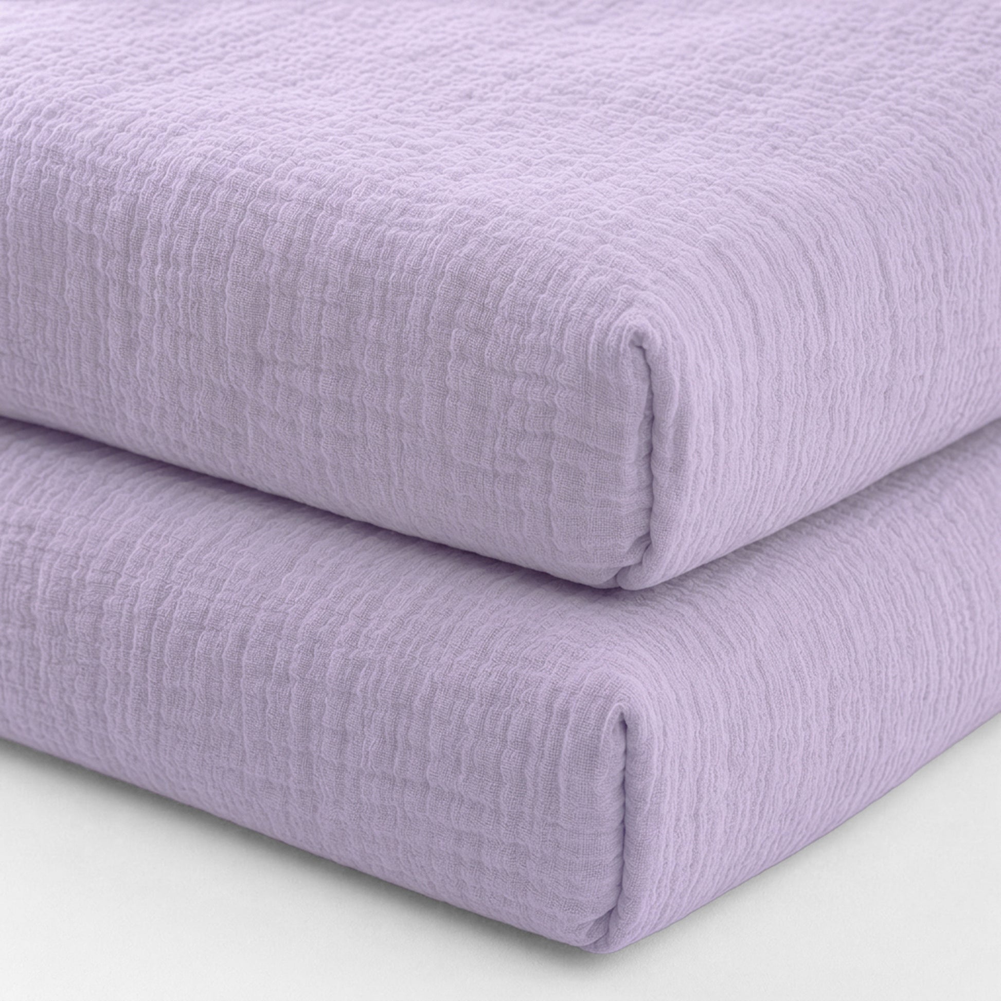 Two breathable, organic cotton sheets (2-pack) by Newton Baby are stacked against a plain white background. Their soft lavender color and textured finish evoke the cozy comfort of premium crib bedding.