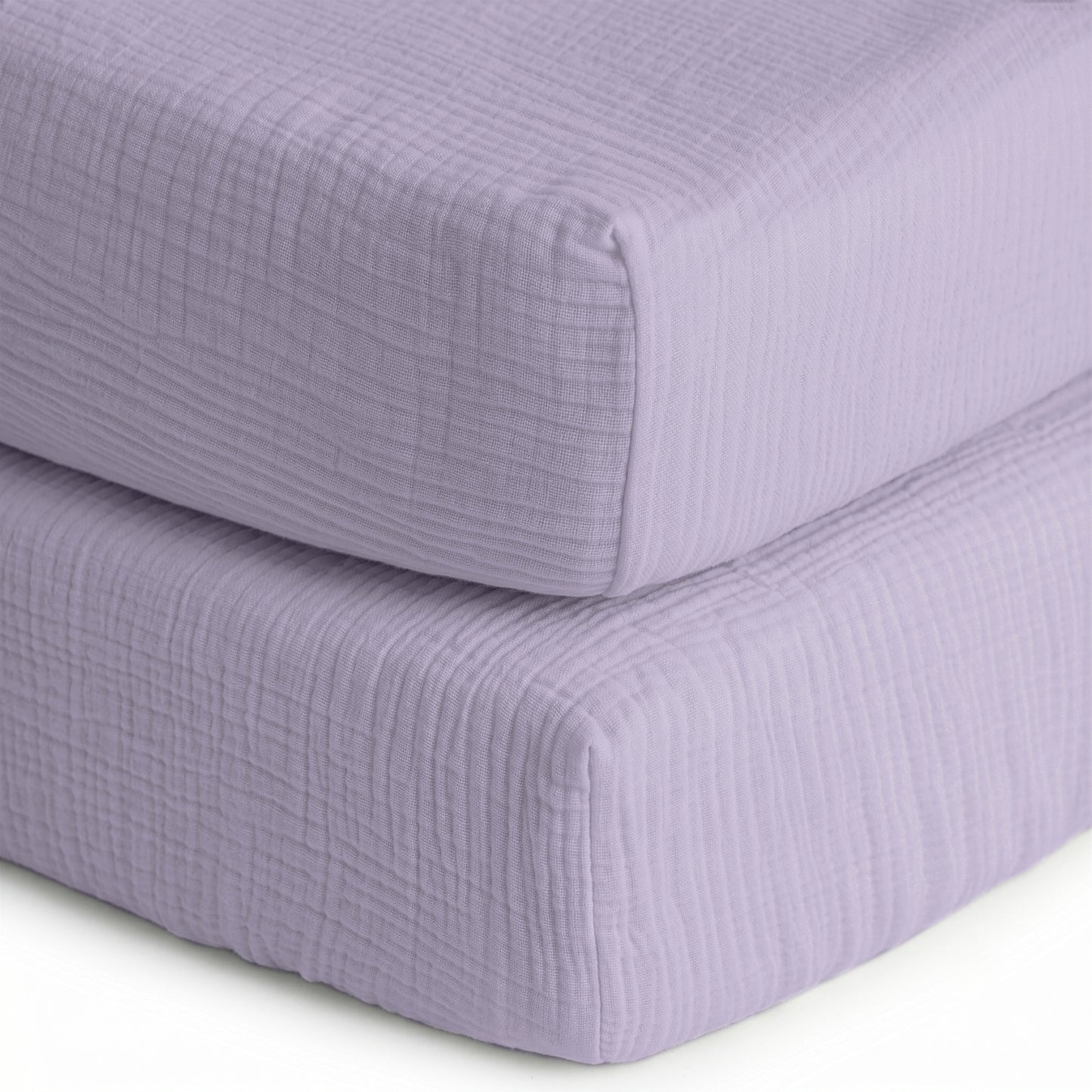 A close-up of two neatly stacked Newton Baby Breathable, Organic Cotton Sheets (2-pack) featuring a textured, muslin-like lavender fabric cover against a white background.