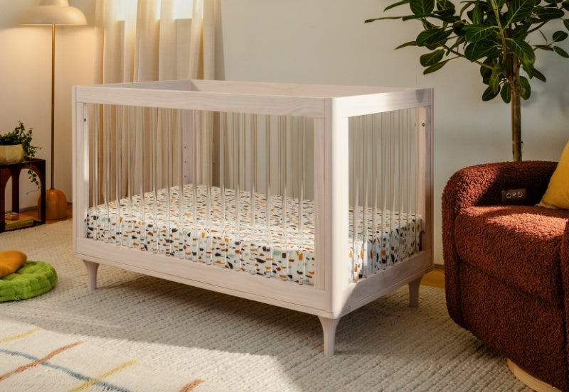 A stylish white crib with a colorful patterned mattress in a warmly decorated nursery room.