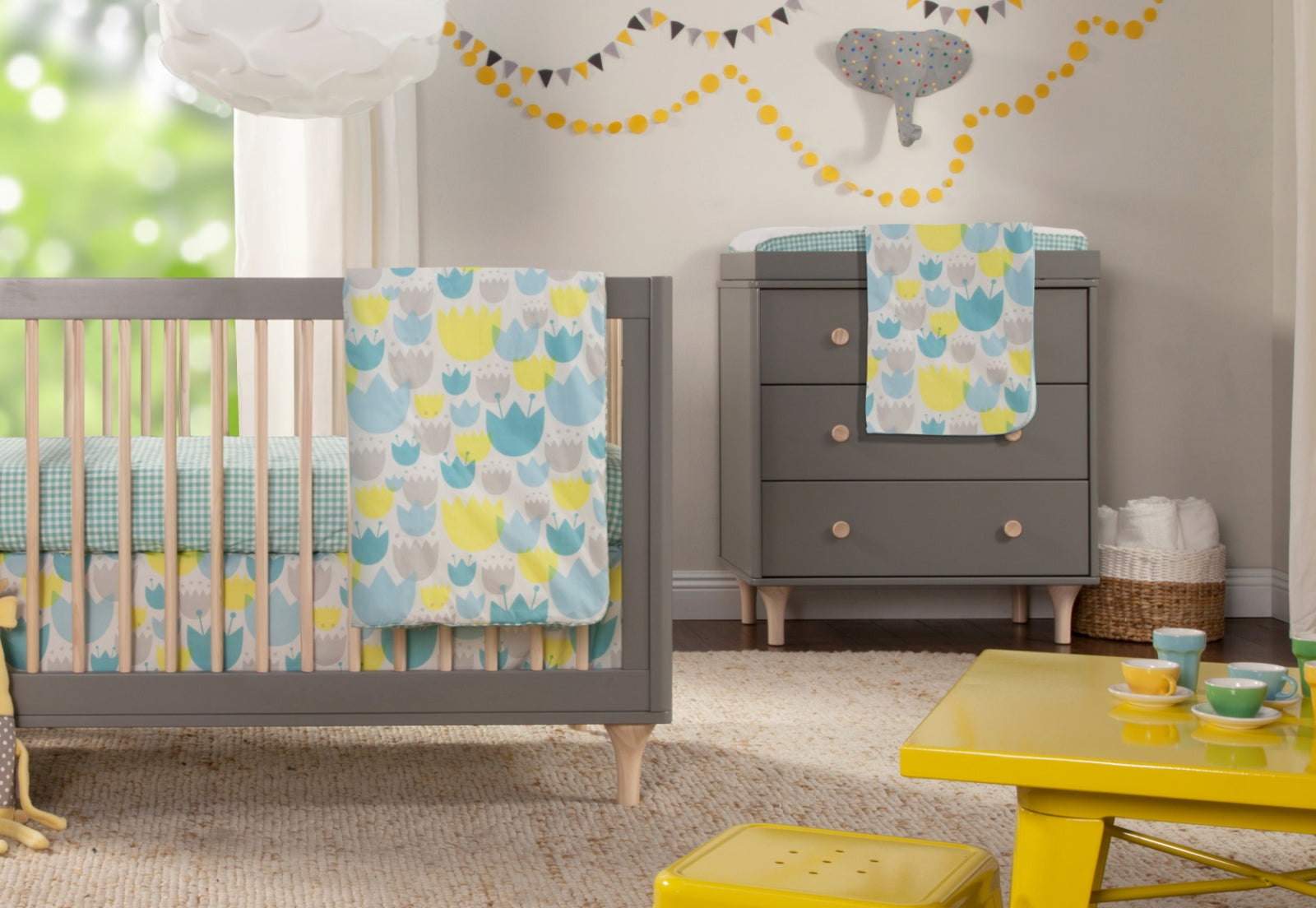 A stylish nursery room featuring a crib and changing table coordinated with blue and yellow patterned linens, under a festive banner, creating a cozy and inviting atmosphere.