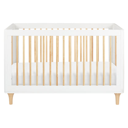 The Babyletto Lolly Convertible Crib features a modern design with a white frame, natural New Zealand pine wood slats, and short angled legs. Shown from the front with a fitted white mattress inside, this crib seamlessly blends style and functionality for your nursery.