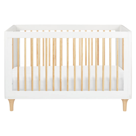 The Babyletto Lolly Convertible Crib features a modern design with a white frame, natural New Zealand pine wood slats, and short angled legs. Shown from the front with a fitted white mattress inside, this crib seamlessly blends style and functionality for your nursery.