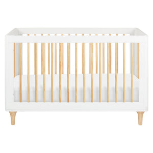 The Babyletto Lolly Convertible Crib features a modern design with a white frame, natural New Zealand pine wood slats, and short angled legs. Shown from the front with a fitted white mattress inside, this crib seamlessly blends style and functionality for your nursery.