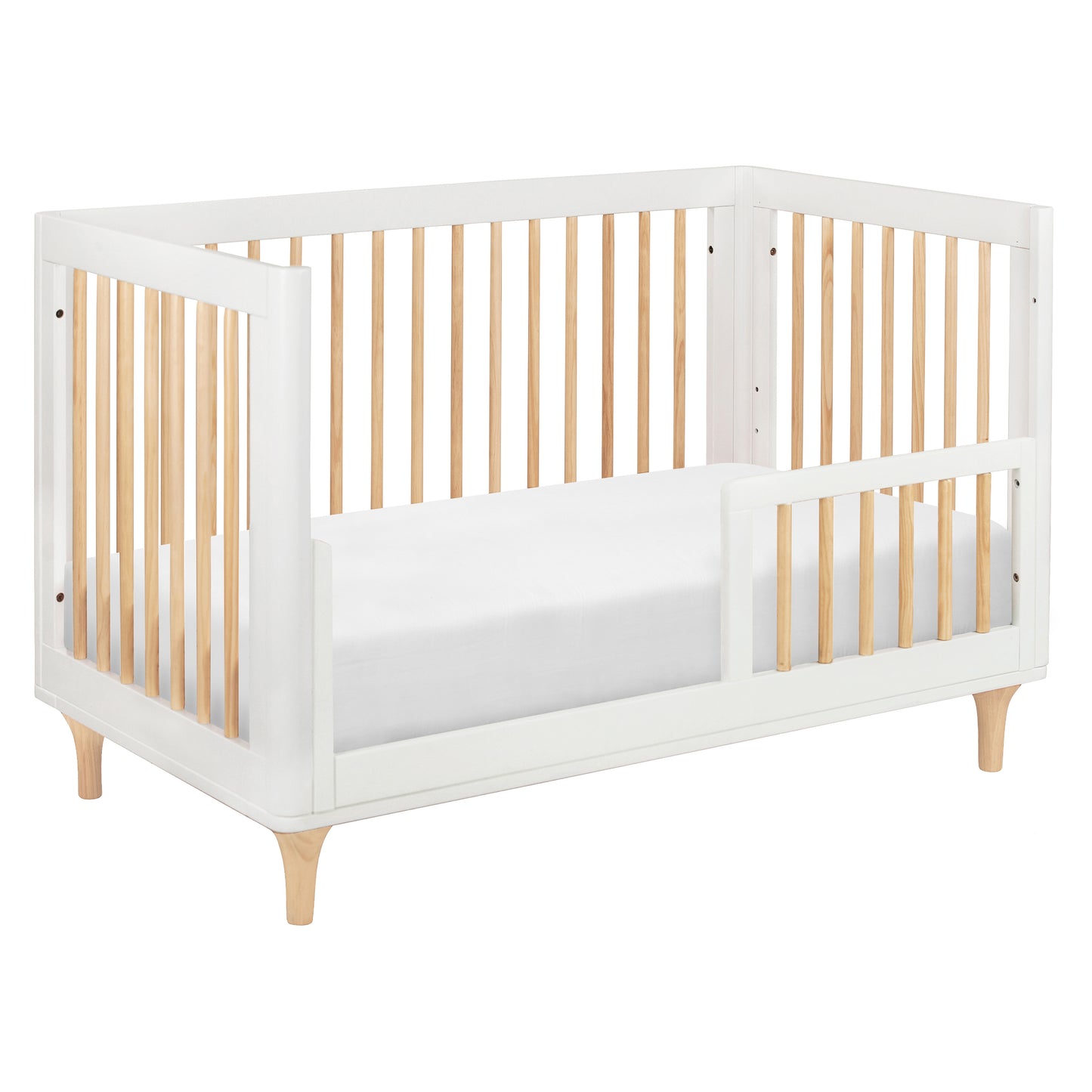 The Babyletto Lolly Convertible Crib features a white and natural wood design, crafted from sustainable New Zealand pine wood with slatted sides, an open section for easy entry, and short angled legs.