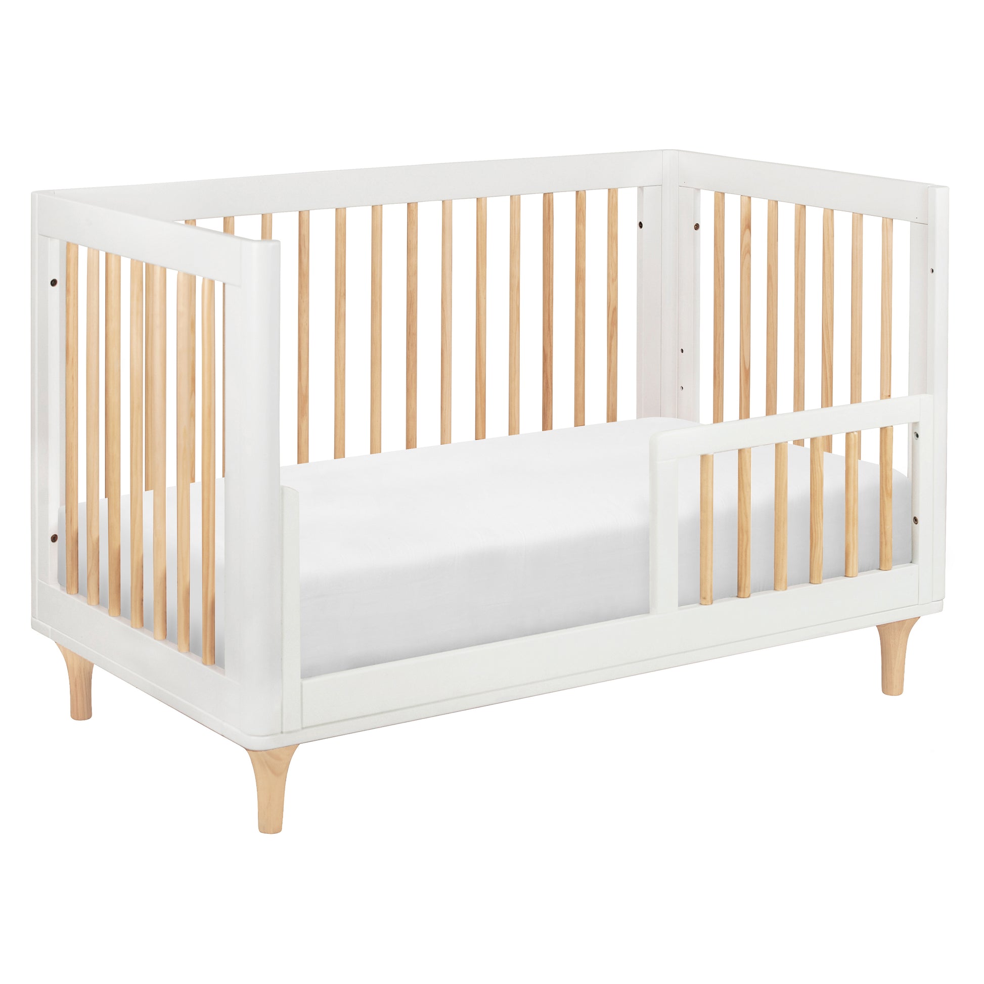 The Babyletto Lolly Convertible Crib features a white and natural wood design, crafted from sustainable New Zealand pine wood with slatted sides, an open section for easy entry, and short angled legs.
