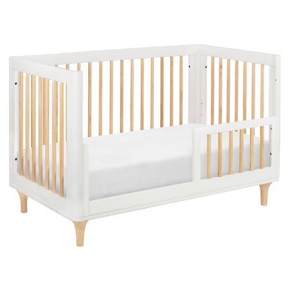 The Babyletto Lolly Convertible Crib features a white and natural wood design, crafted from sustainable New Zealand pine wood with slatted sides, an open section for easy entry, and short angled legs.