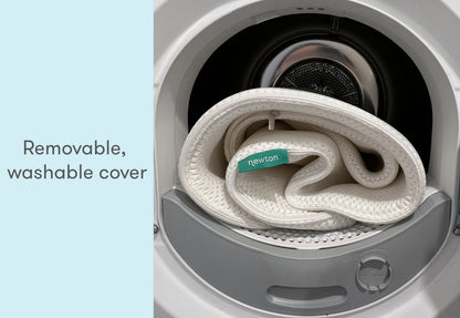 A removable, washable Newton baby mattress cover coiled inside a washing machine, with text "Removable, washable cover" displayed at the top.