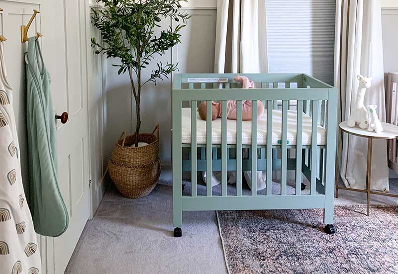 A cozy nursery featuring a mint green crib with a baby inside, surrounded by a serene decor with a plant, a patterned blanket, and soft lighting.