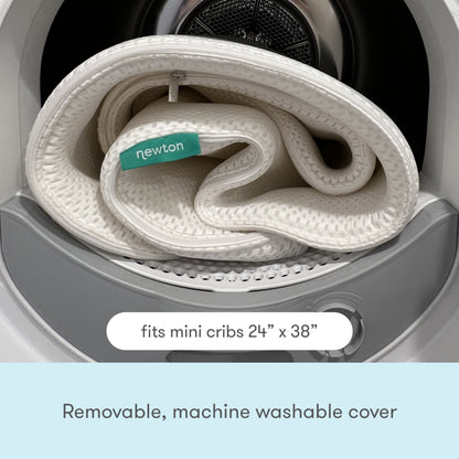 A removable, washable Newton baby mattress cover coiled inside a washing machine, with text "Removable, washable cover" displayed at the top. 