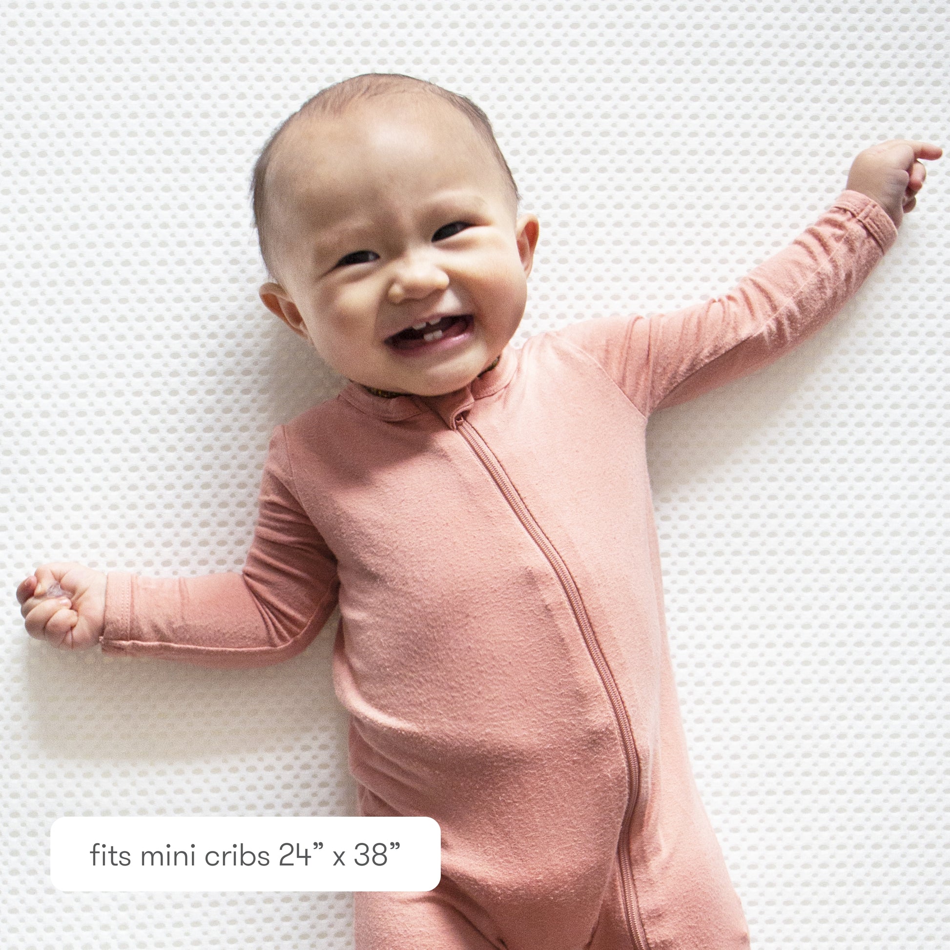 Smiling baby bundled in a floral outfit  against a textured background with text "fits mini cribs 24" x 38" 