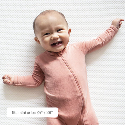 Smiling baby bundled in a floral outfit  against a textured background with text "fits mini cribs 24" x 38" 