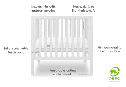 White modern crib on wheels with visible mattress, isolated on a plain background. Callouts with text, "newton mini crib mattress included," "Non-toxic, lead & phthalate-safe," "Heirloom quality & construction," "solid, sustainable beech wood," "removable locking caster wheels." PEFC certified.