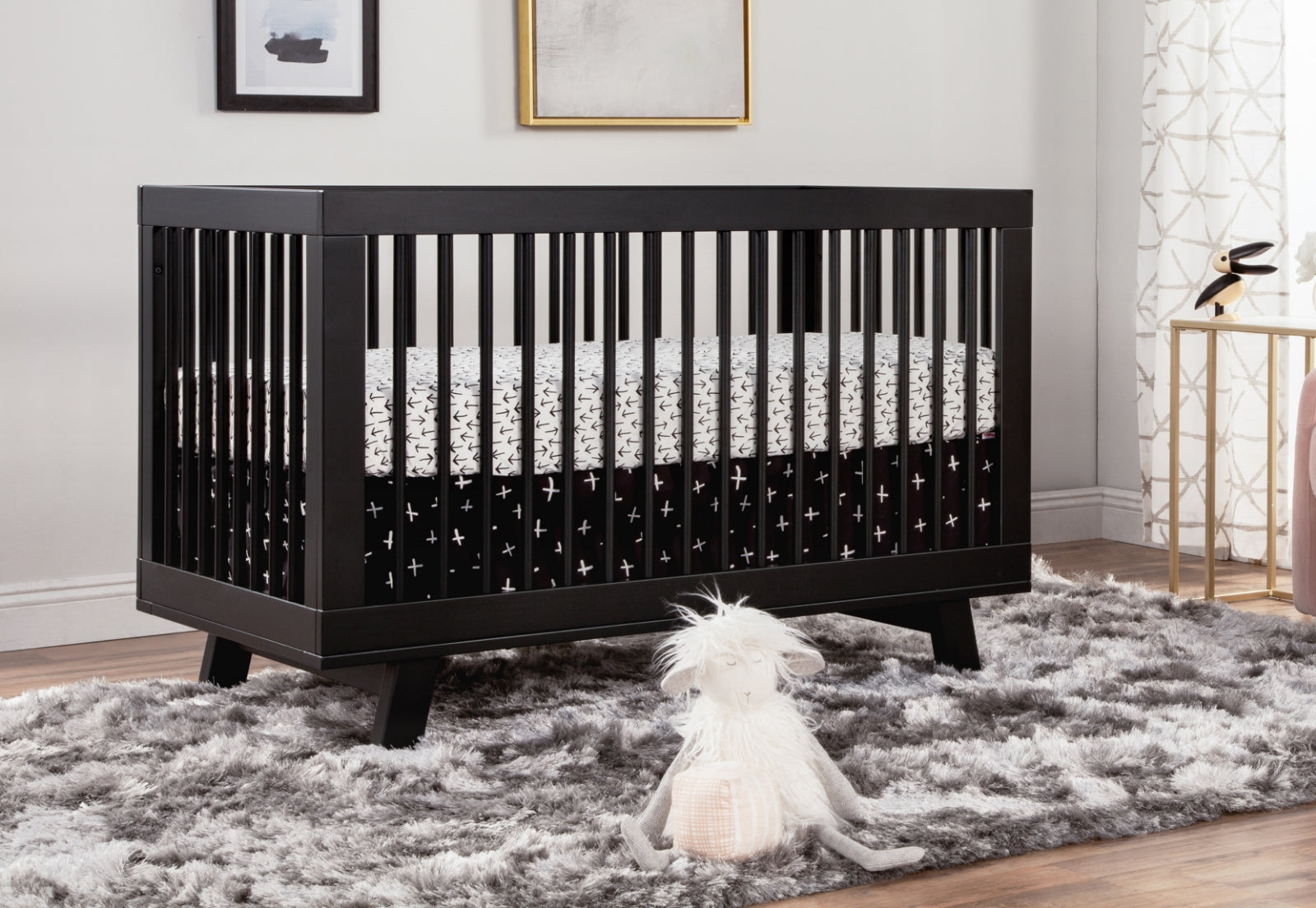 Elegant black crib with white accent bedding and plush animal toy on a shaggy grey rug, set against a chic, modern room decor. 999-8501-BLK