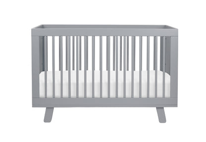 Gray modern baby crib with white mattress isolated on a white background.