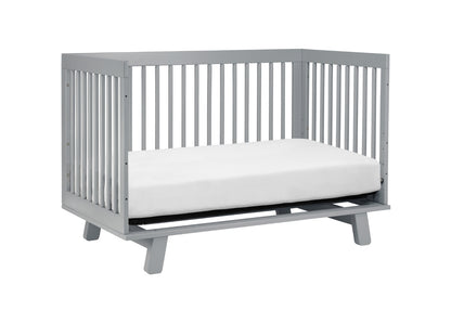 Gray modern baby crib with a white mattress on a plain background.