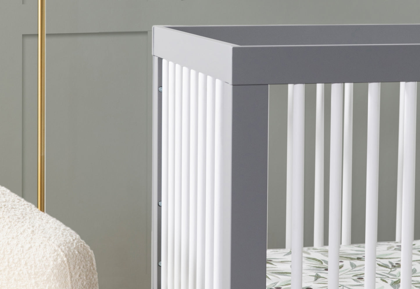 Close-up view of a stylish gray baby crib in a nursery with a cream blanket visible on the side.