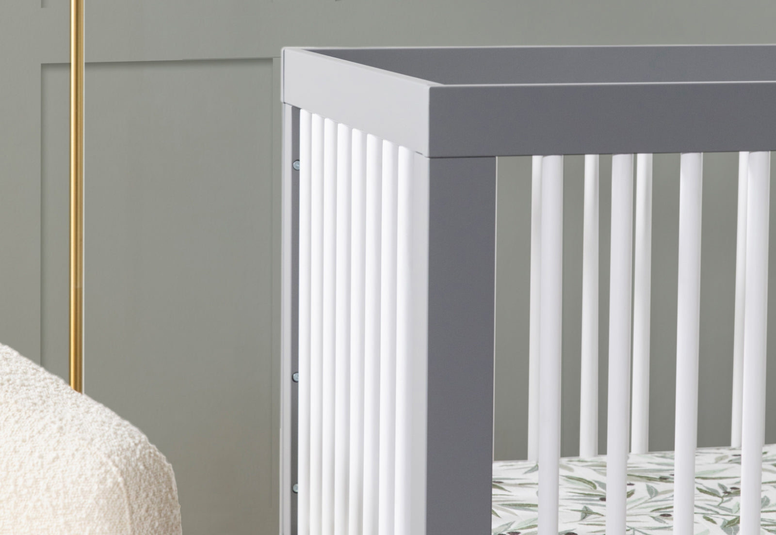Close-up view of a stylish gray baby crib in a nursery with a cream blanket visible on the side.