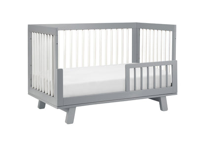 Gray modern baby crib with a white mattress, isolated on a white background.