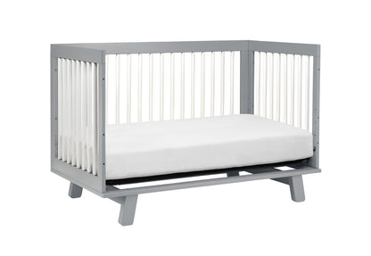 Gray modern baby crib with a white mattress, isolated on a white background.