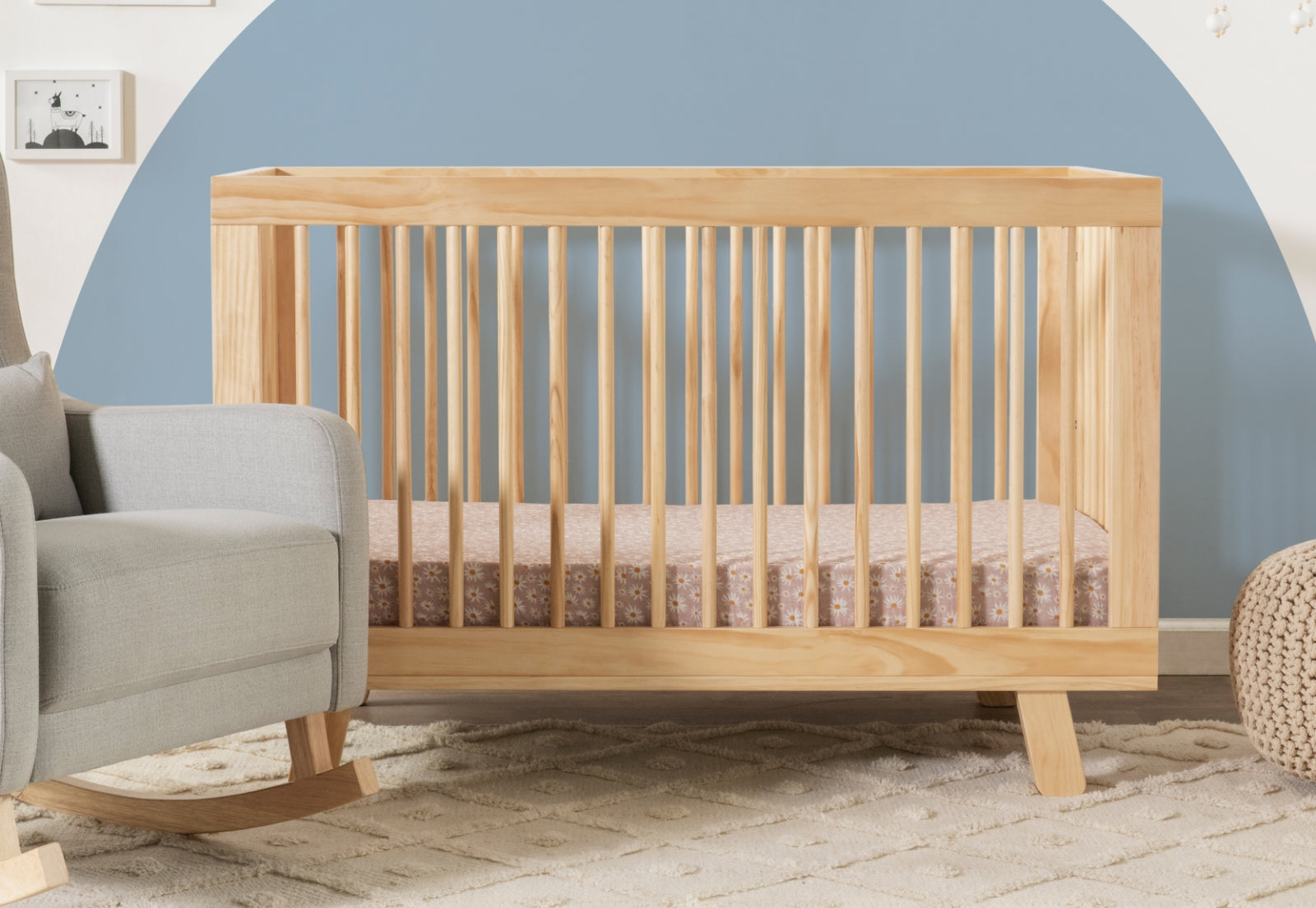 Modern wooden crib in a nursery with blue and white walls, next to a grey armchair and on a textured cream carpet. 999-8501-NAT