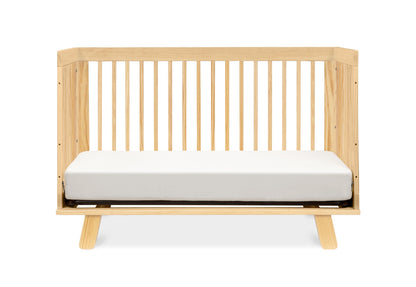 Contemporary wooden crib with a white mattress against a plain background.