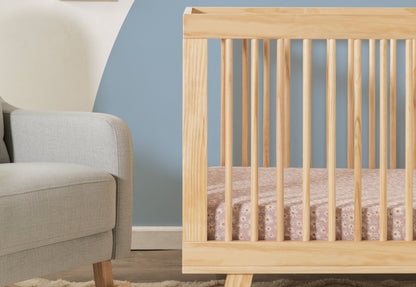 Wooden crib with visible grain beside a modern gray armchair, set against a two-tone wall of cream and blue.