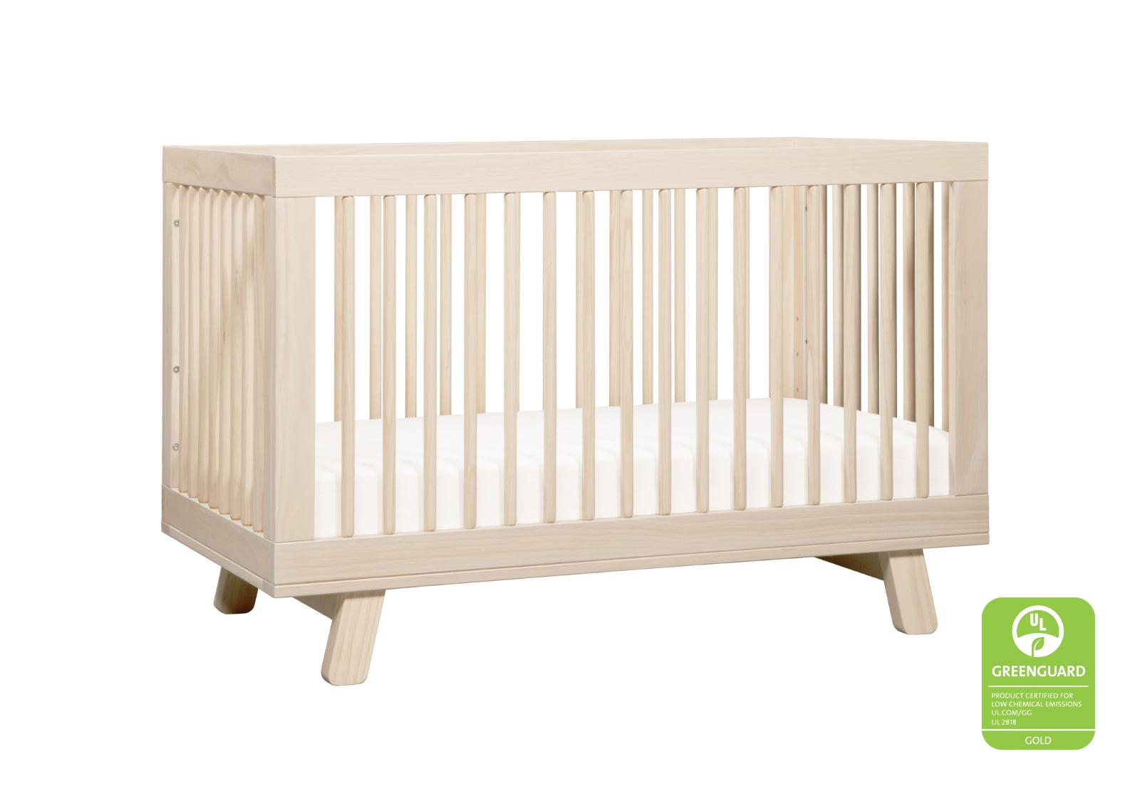 Light wooden baby crib with white bedding, featuring a GREENGUARD Gold Certification for low chemical emissions.