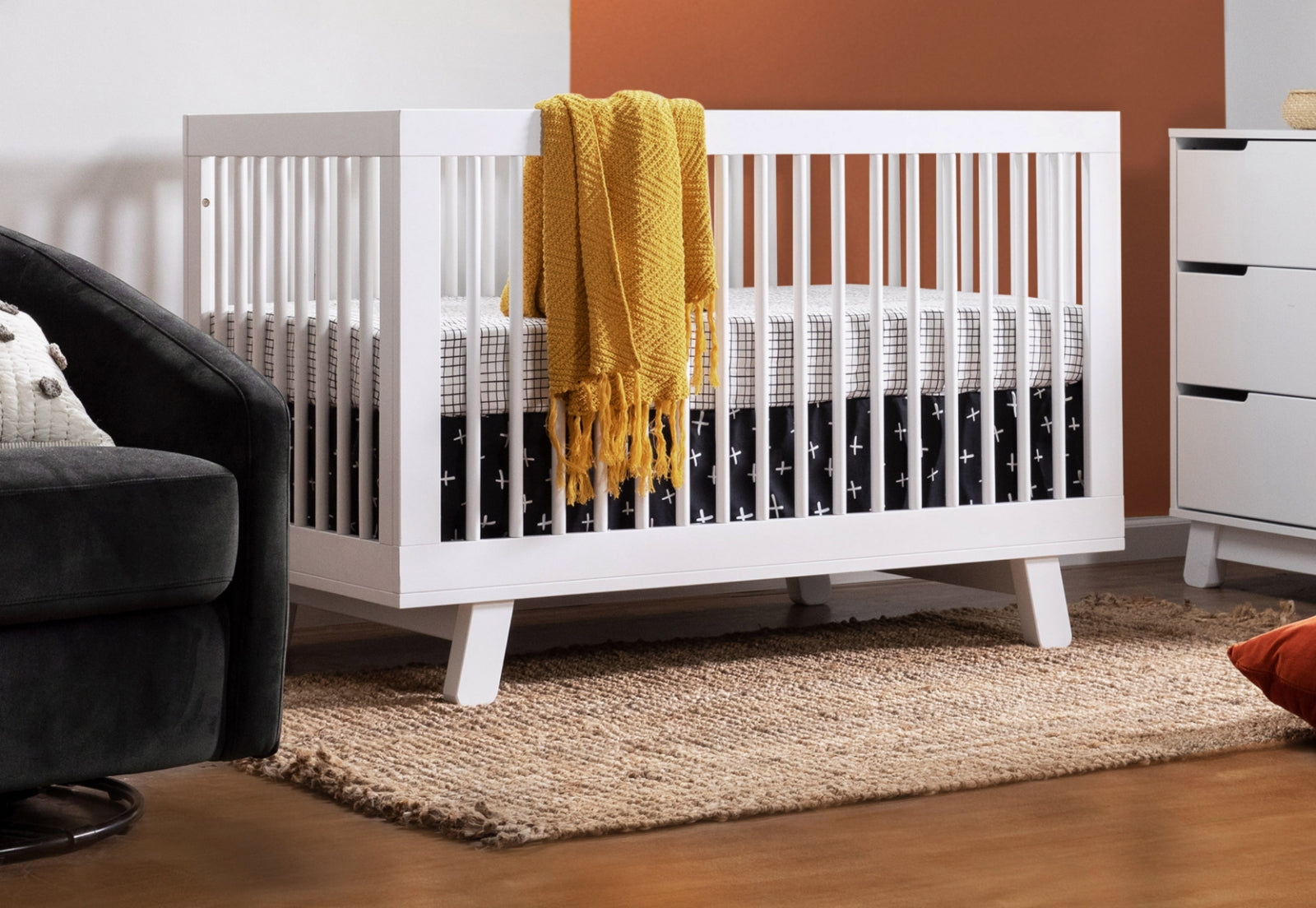 A stylish white crib with a yellow throw blanket inside a modern nursery room setting.
