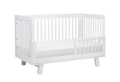A modern white baby crib with stylish slatted design and a lowered front rail on a plain background, ideal for a contemporary nursery.