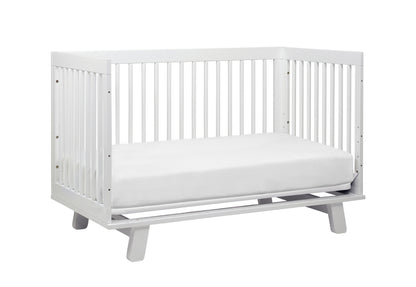 White modern baby crib with a simple design and sturdy slats on a gray base.