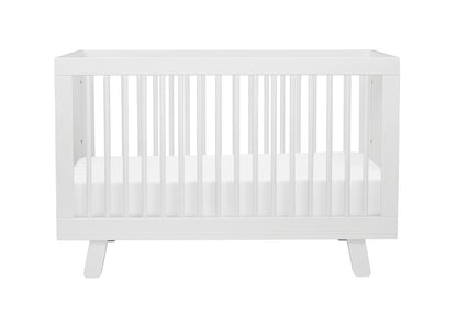 A modern white baby crib with a simple design and sturdy slats, isolated on a white background.
