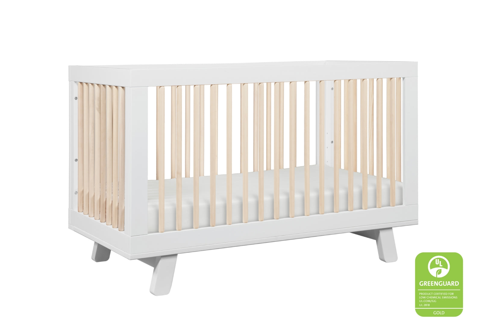 Modern white baby crib with natural wood spindles, featuring a Greenguard Gold certification sticker.