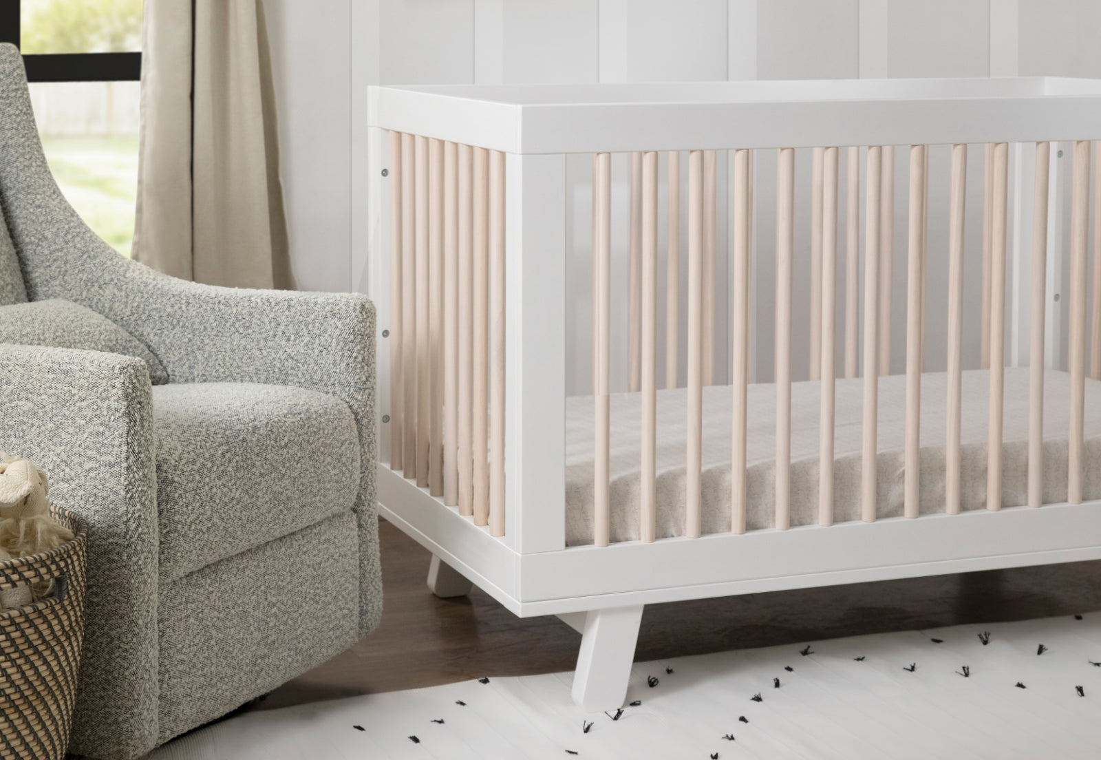 A serene nursery featuring a modern white crib with beige bedding, complemented by a cozy gray armchair and neutral-toned curtains.