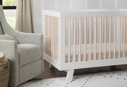 A serene nursery featuring a modern white crib with beige bedding, complemented by a cozy gray armchair and neutral-toned curtains.