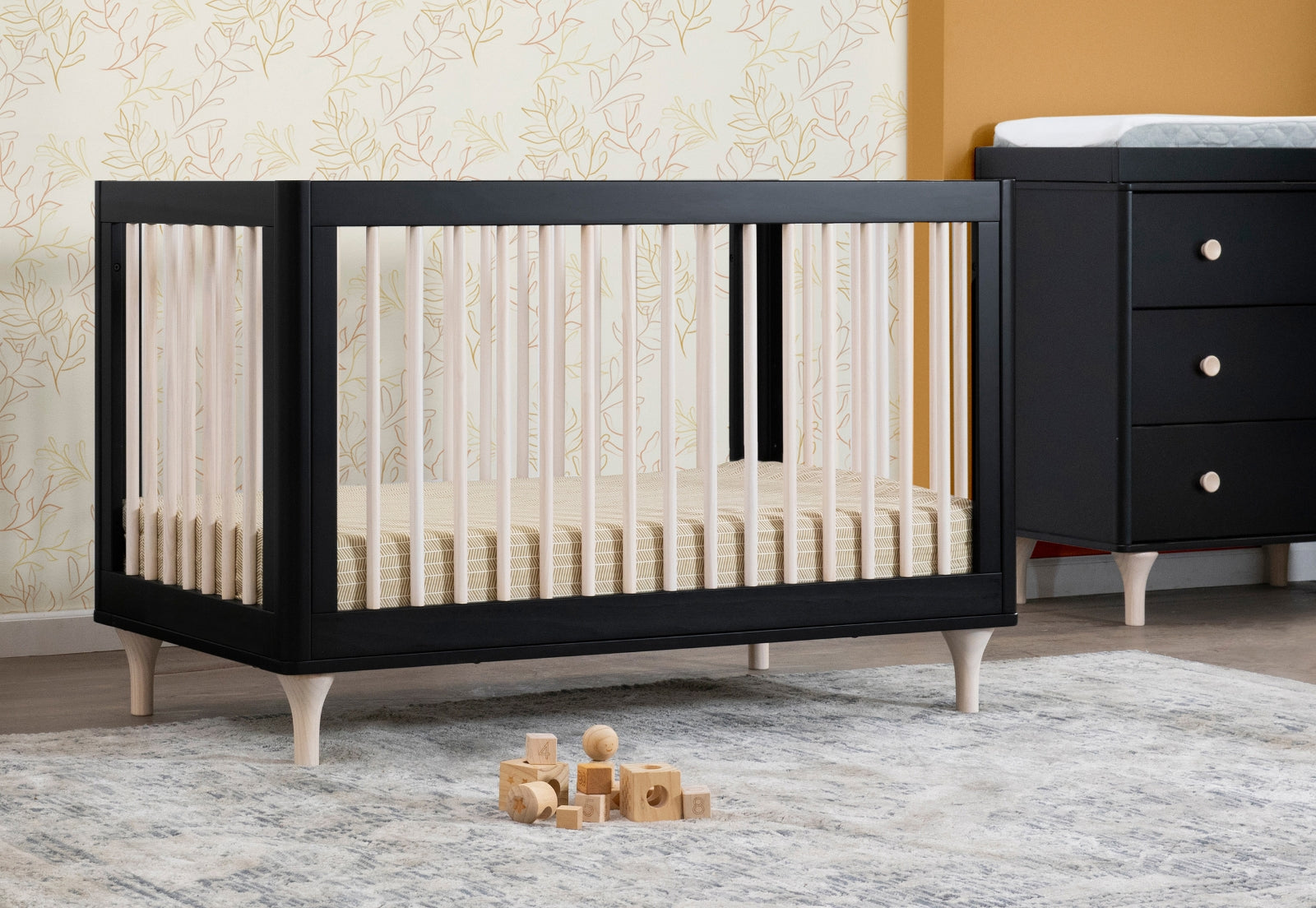 Elegant black nursery crib with a matching dresser on a serene wallpaper background, decorated with wooden block toys. 999-8502-BWN