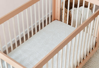 Wooden baby crib with light cream and gray patterned mattress in a softly lit room, providing a comfortable and stylish sleeping environment for infants.