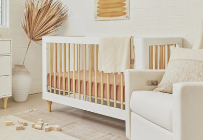Cozy nursery room with a modern white crib draped with a beige blanket, a comfortable armchair, and soft blocks on the floor, adorned with natural decor elements.