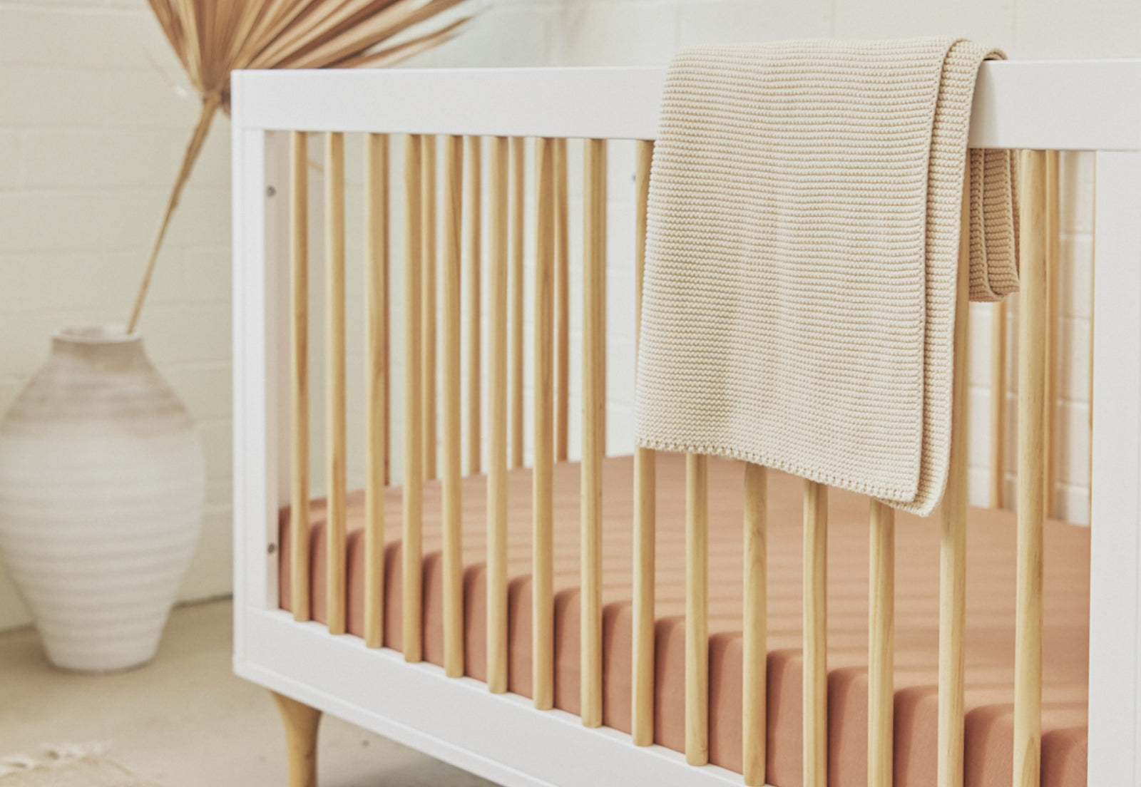 A cozy beige baby blanket draped over the side of a white crib in a softly decorated nursery.